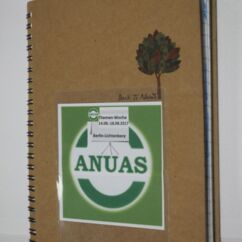 Ein braunes Notizbuch mit dem ANUAS Logo