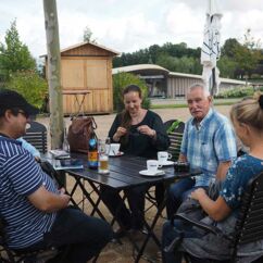 vier Personen sitzen an einem Gartentisch im Freien und trinken Kaffee