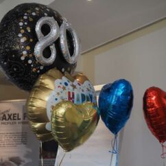 Verschiedene bunte Luftballons, ein Luftballon trägt die Zahlen 80