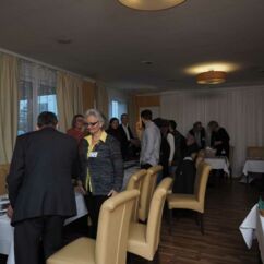 viele Menschen nehmen an einem langen Tisch in einem Tagungsraum Platz