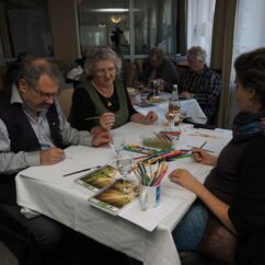mehrere Personen sitzen an einem Tisch und malen auf Papierblättern