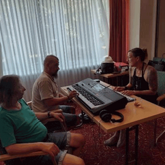 Drei Personen sitzen um ein Keyboard, eine Person spielt auf dem Keyboard