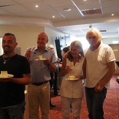 Mehrere Personen stehen mit Kuchentellern in der Hand und lächeln