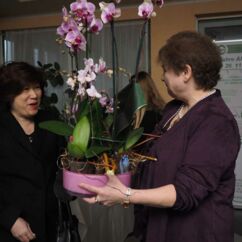 eine Frau überreicht einer anderen Frau eine Schale mit Ochideen