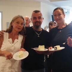 Drei Personen mit Kuchentellern in der Hand lächeln in die Kamera